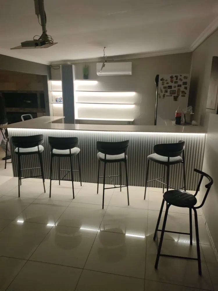 A kitchen peninsula with a fluted front lit by a strip light underneath, with backlit recessed shelves on the wall behind.